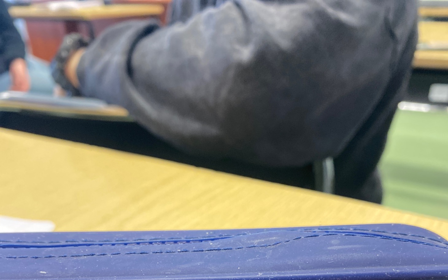 
        Fragment stołu z osobą w tle, siedzącą na krześle.
    