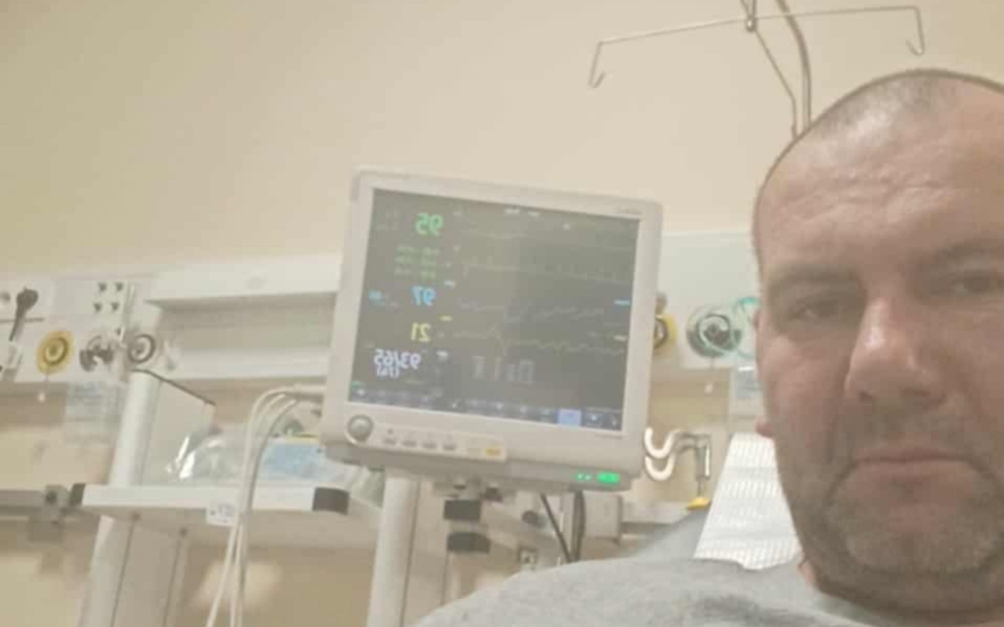 
        Mężczyzna w szpitalu, z monitorami medycznymi w tle, wygląda na zmartwionego.
    