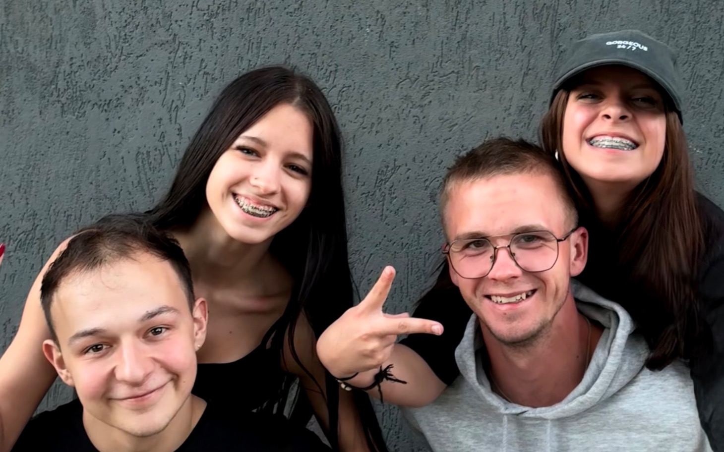 
        Grupa młodych ludzi pozujących razem na tle szarej ściany.
    