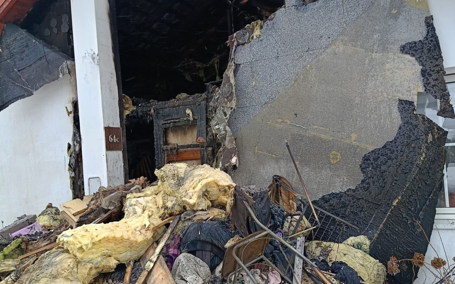 
        Zniszczona ściana budynku po pożarze, widoczne odpady.
    