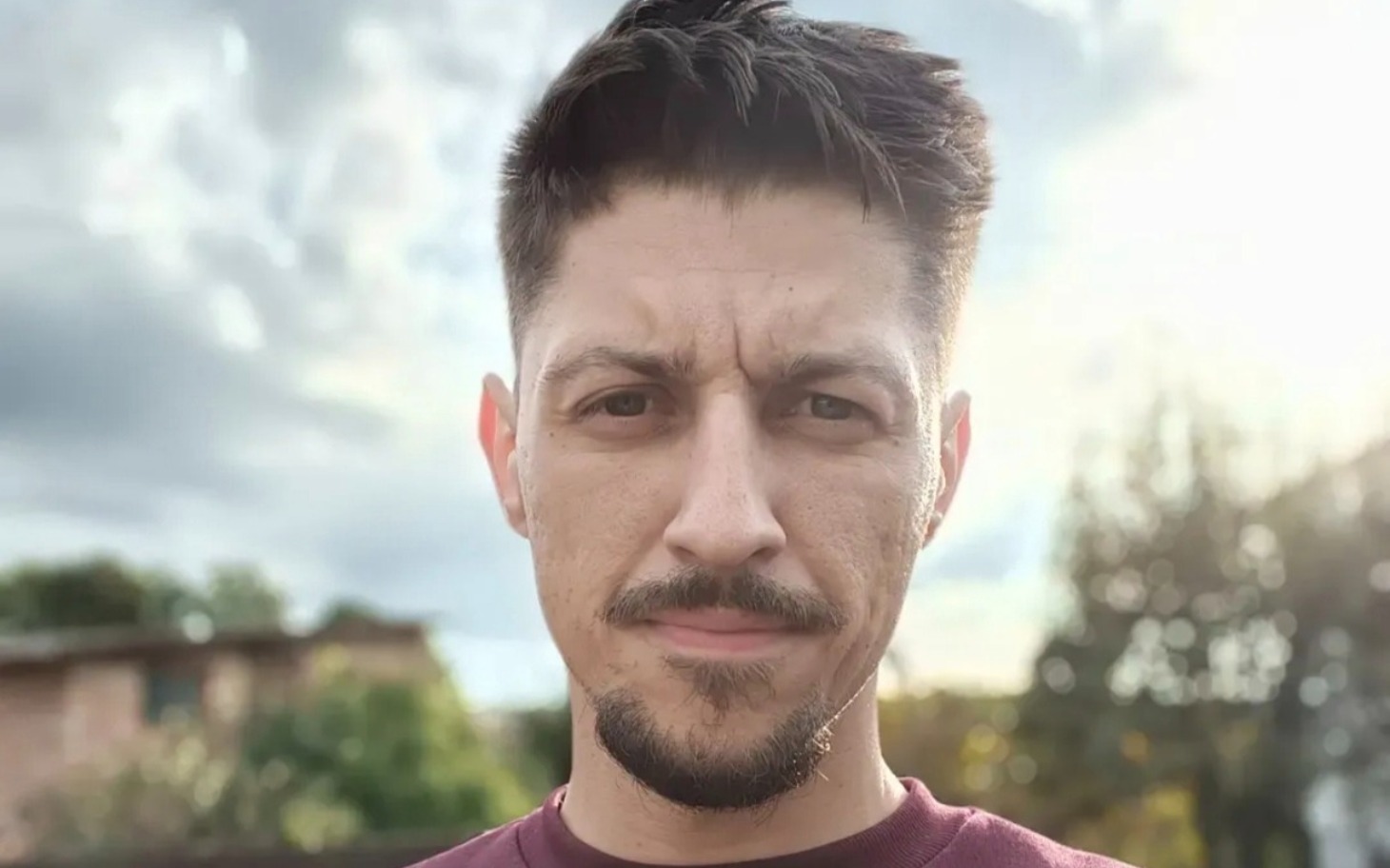 
        Mężczyzna na tle zieleni, z uśmiechem na twarzy.
    