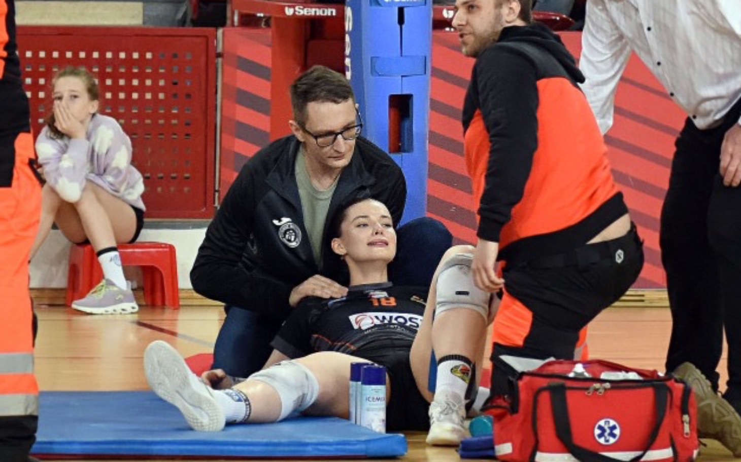 
        Zawodniczka siatkówki na boisku, otrzymuje pomoc medyczną.
    