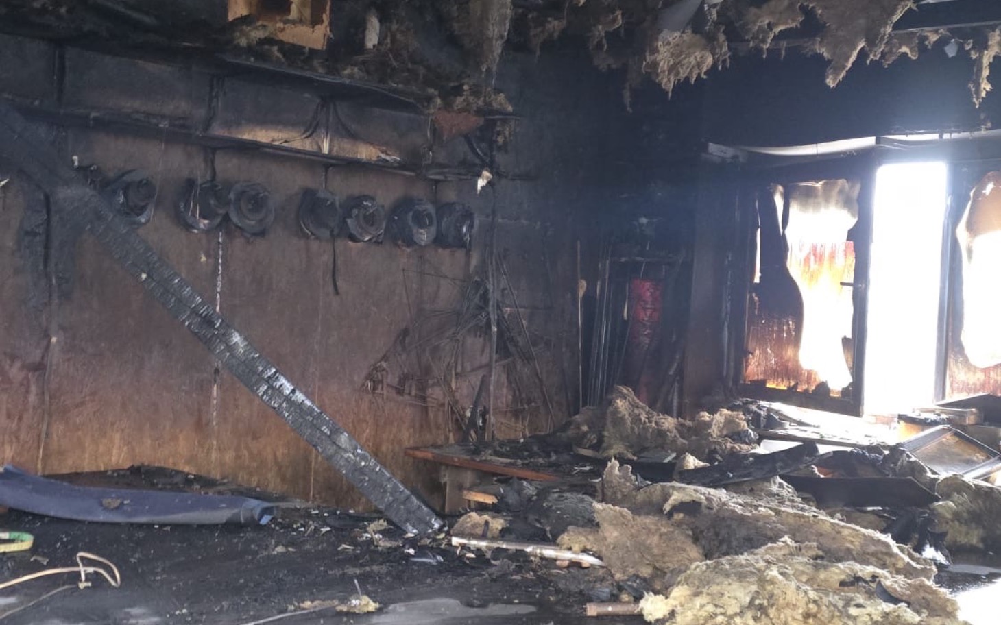 
        Zniszczone wnętrze po pożarze, z uszkodzonymi ścianami i sprzętem.
    