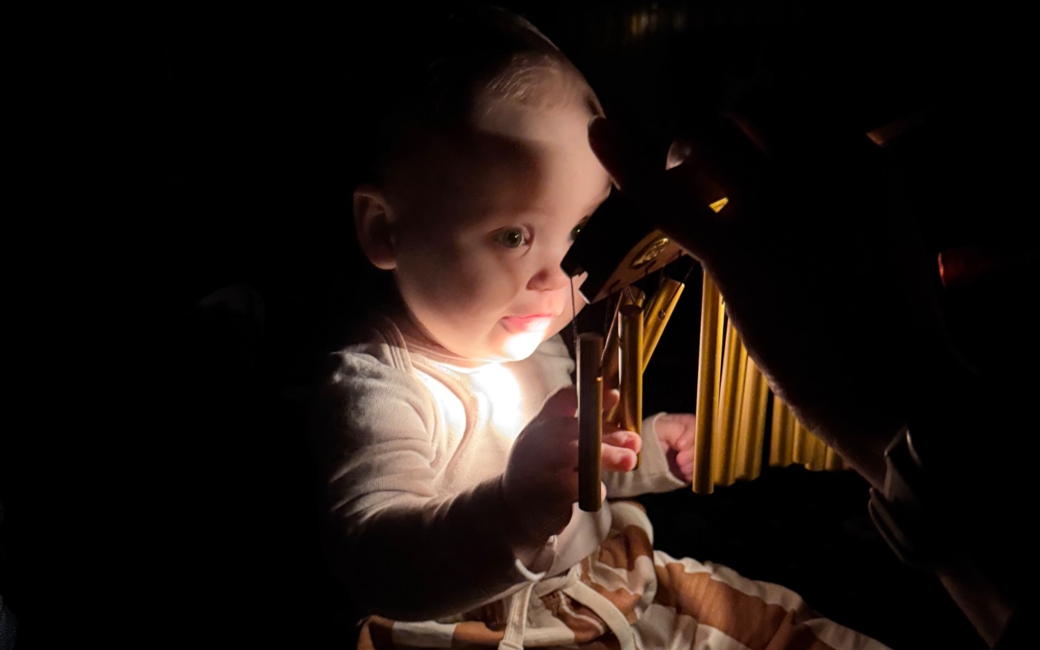 
        Dziecko bawi się zabawką w ciemności, oświetlone delikatnym światłem.
    