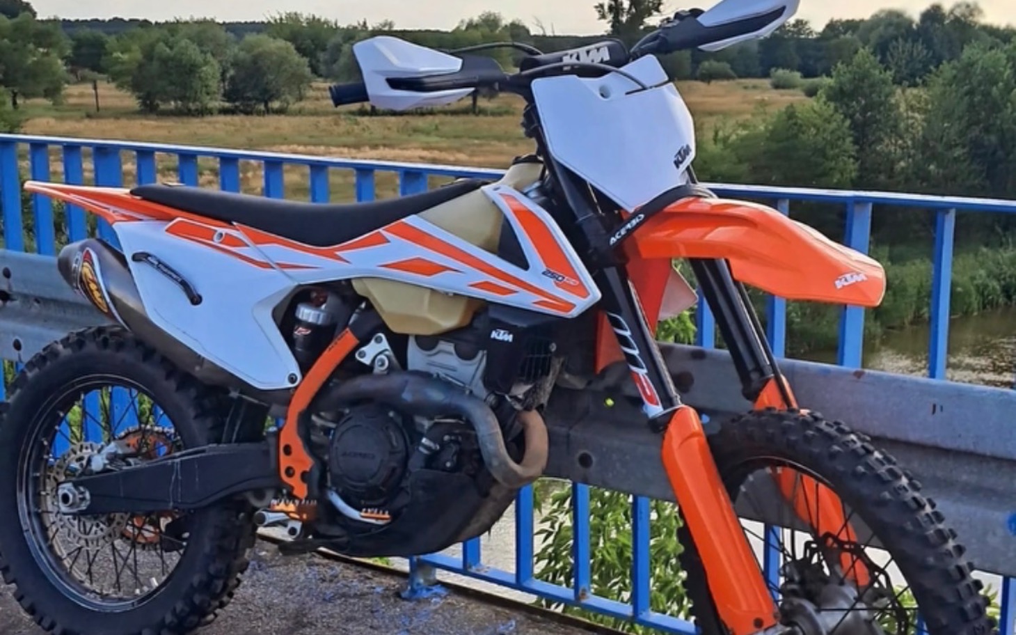 
        Motocykl terenowy na tle zieleni, gotowy do jazdy.
    