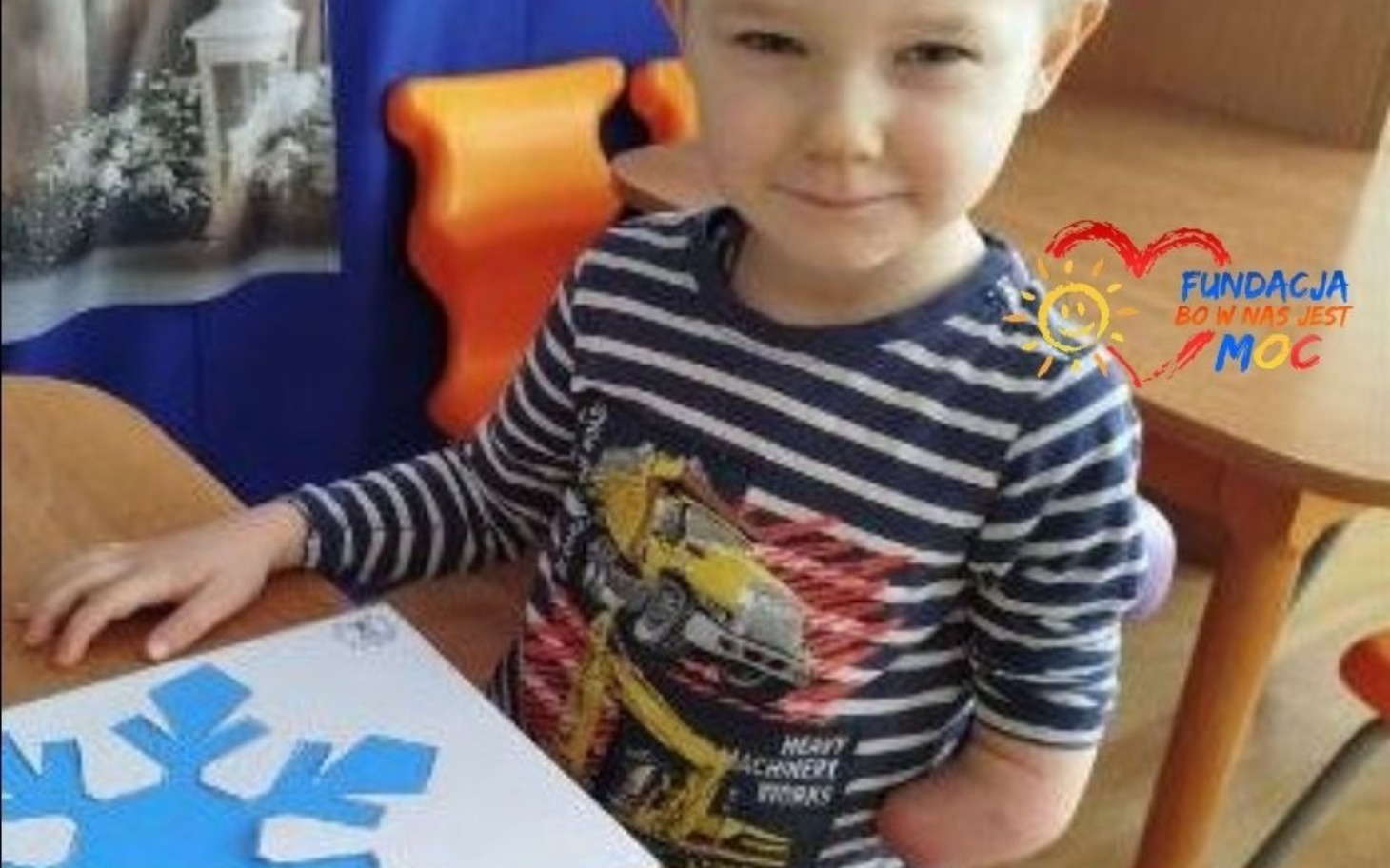 
        Chłopiec z uśmiechem, trzymając kolorowy papier.
    