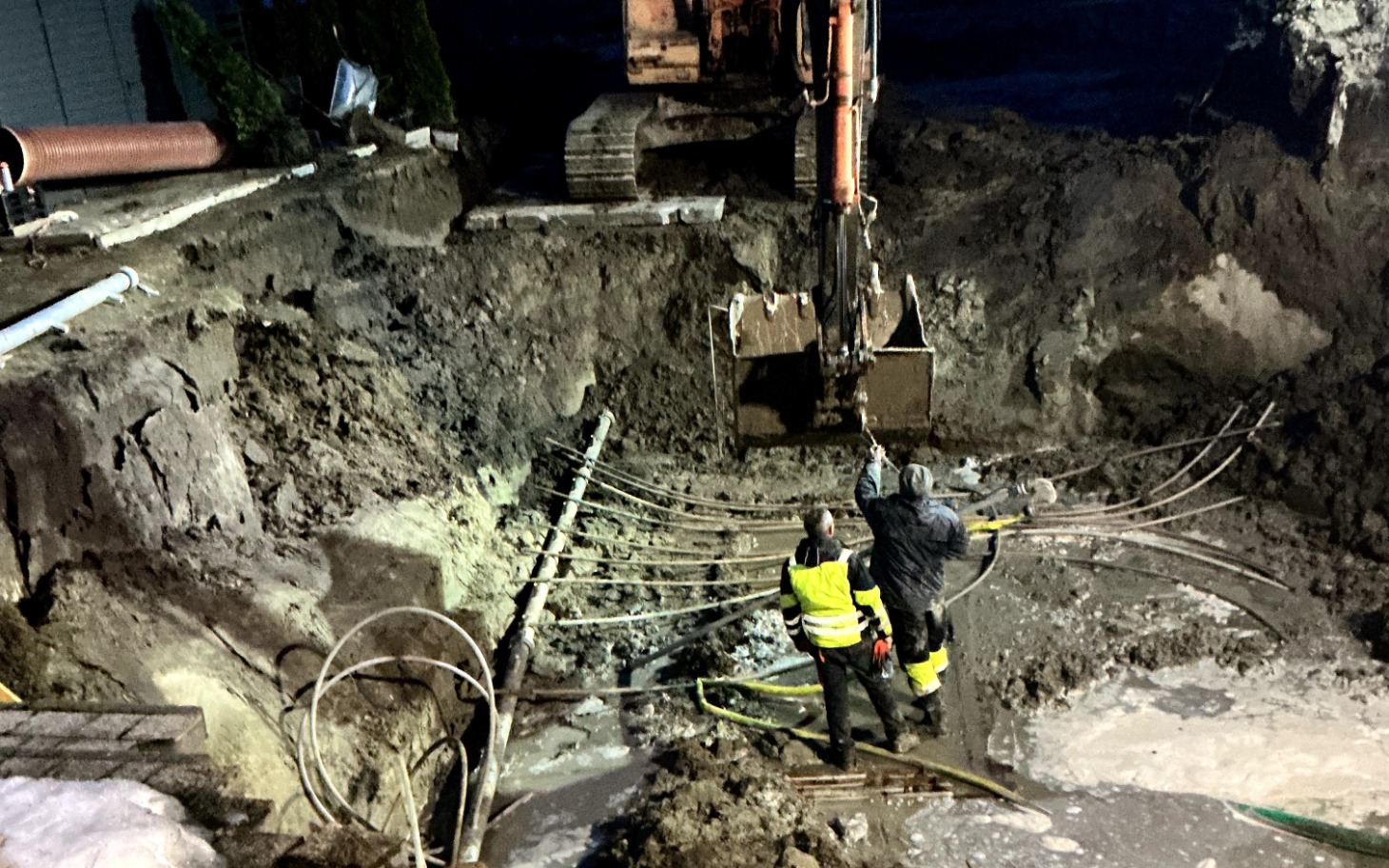 
        Ekipa budowlana pracująca w wykopie, z maszyną w tle.
    