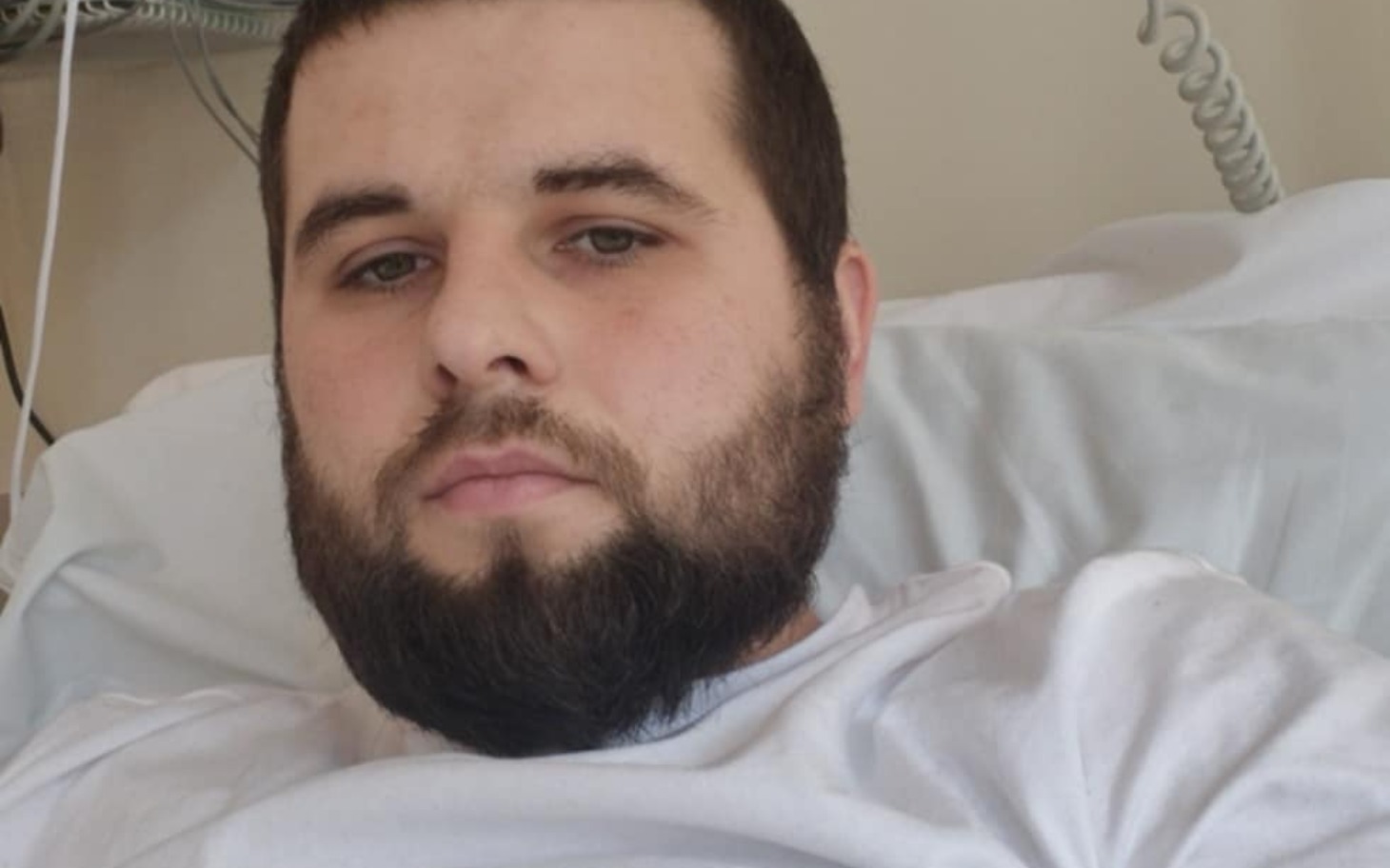 
        Mężczyzna leżący w szpitalnym łóżku, z poważnym wyrazem twarzy.
    