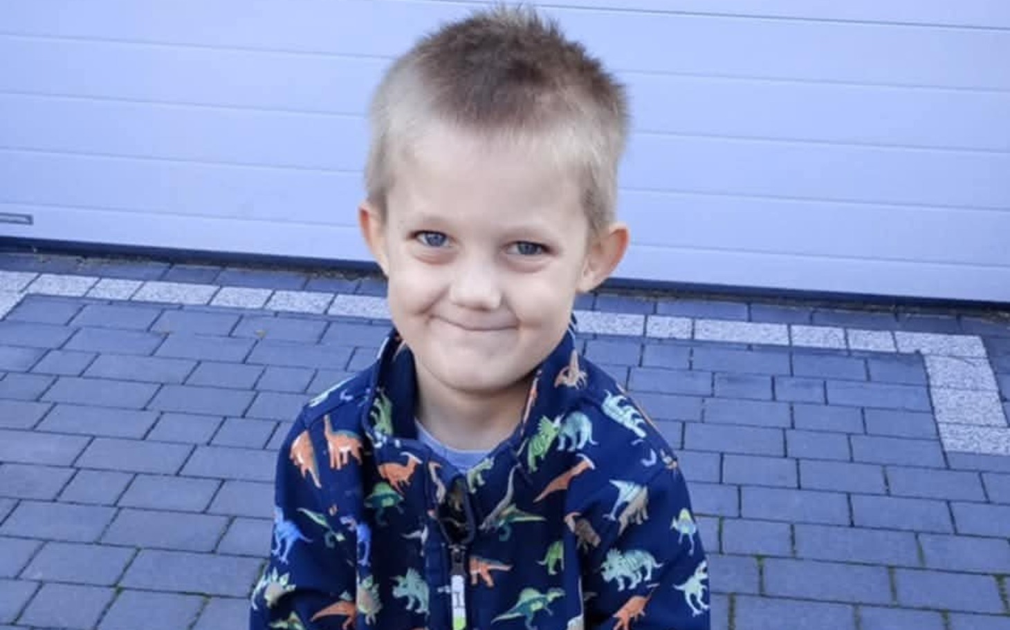 
        Chłopiec uśmiechający się na tle kostki brukowej.
    