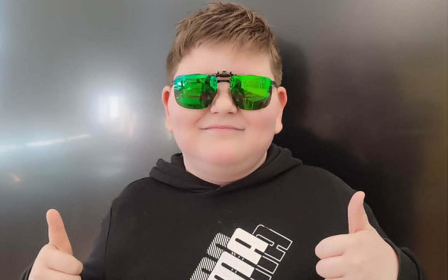 
        Chłopiec w okularach przeciwsłonecznych, pokazujący kciuki w górę.
    