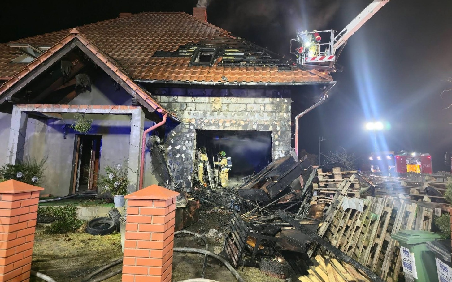 
        Zniszczony dom po pożarze, strażacy w akcji.
    