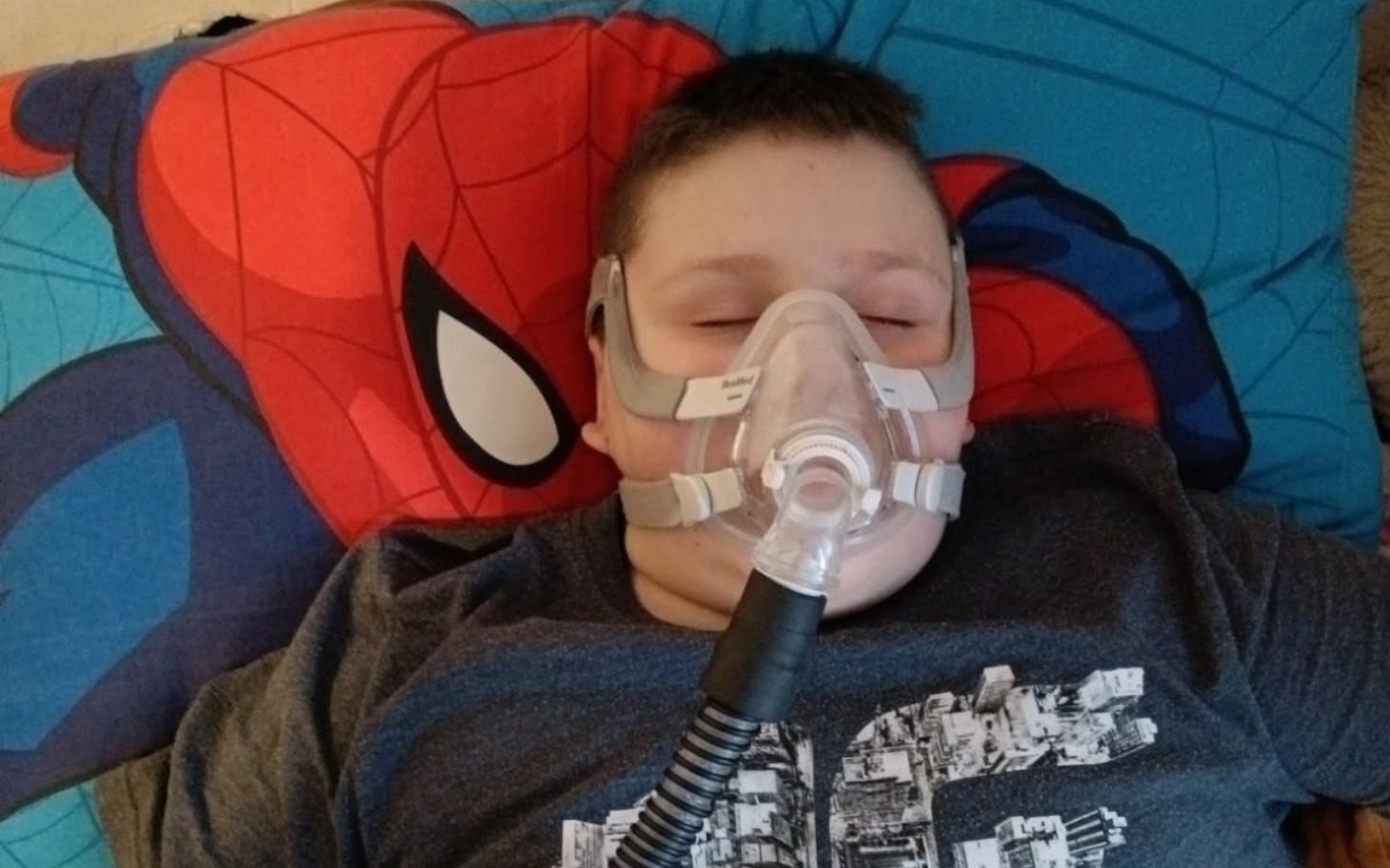 
        Chłopiec z maską tlenową leżący na łóżku.
    