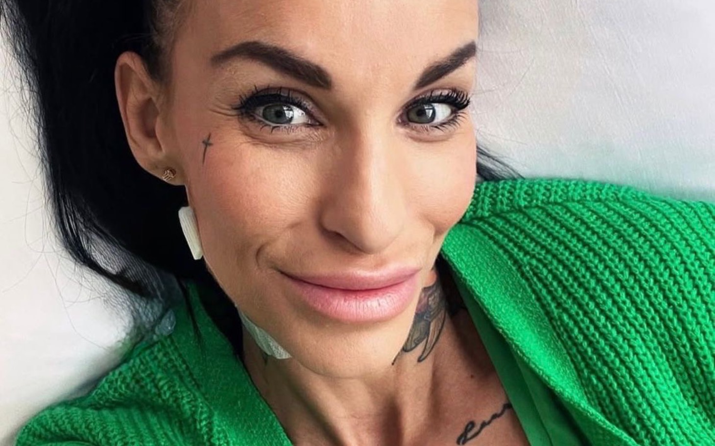 
        Uśmiechnięta kobieta z tatuażami w zielonym swetrze.
    