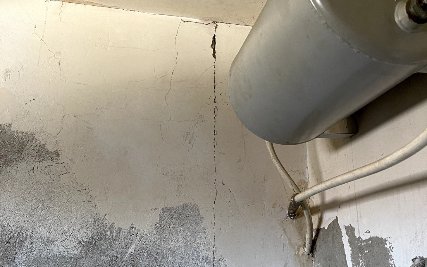 
        Zniszczona ściana w pomieszczeniu, z pęknięciami i wilgocią.
    