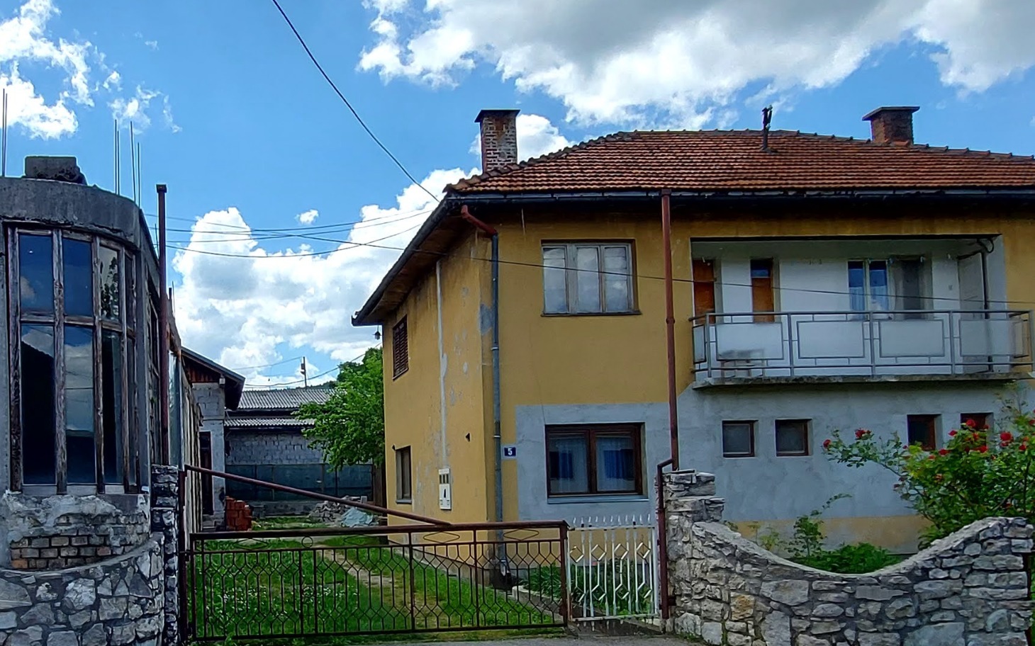 Dom z ogrodem, jasne niebo i chmury w tle.