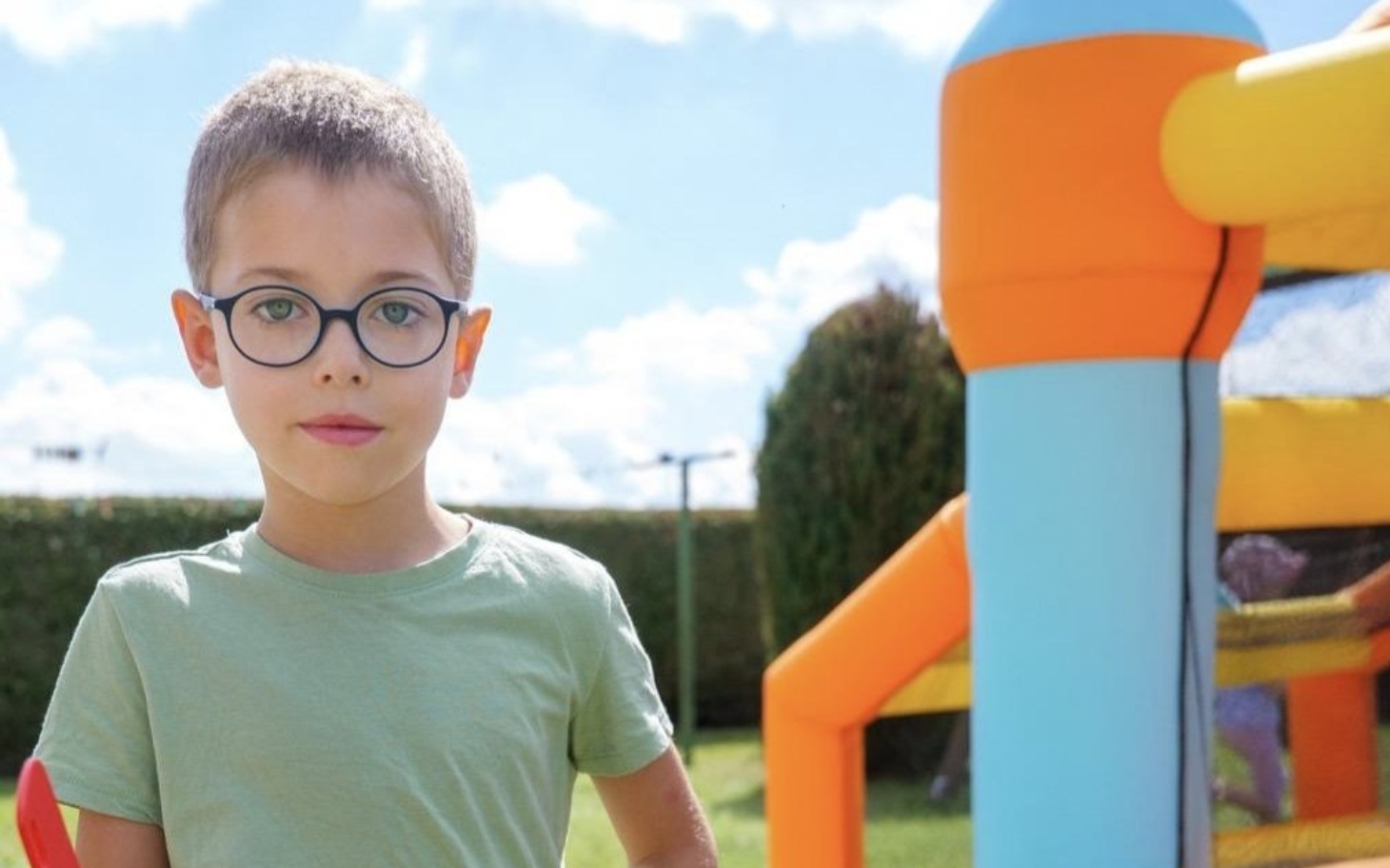
        Chłopiec w okularach stoi obok dmuchanego zamku.
    