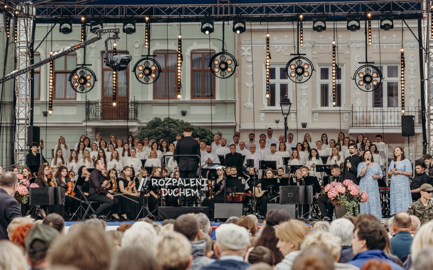 
        Koncert na świeżym powietrzu z chórem i orkiestrą na scenie.
    