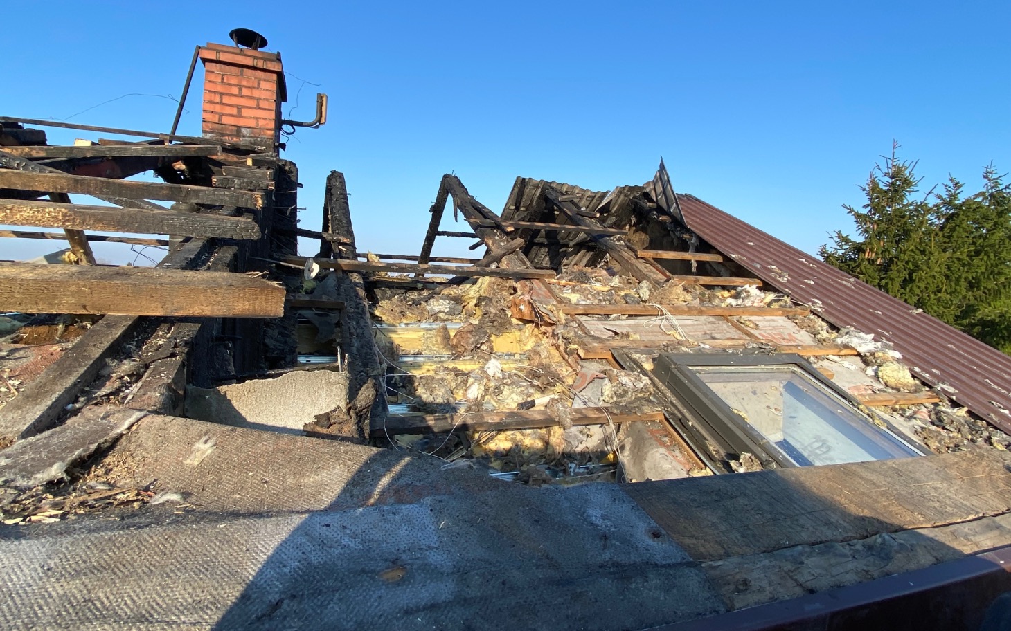 
        Zniszczony dach budynku, widoczne uszkodzenia po pożarze.
    