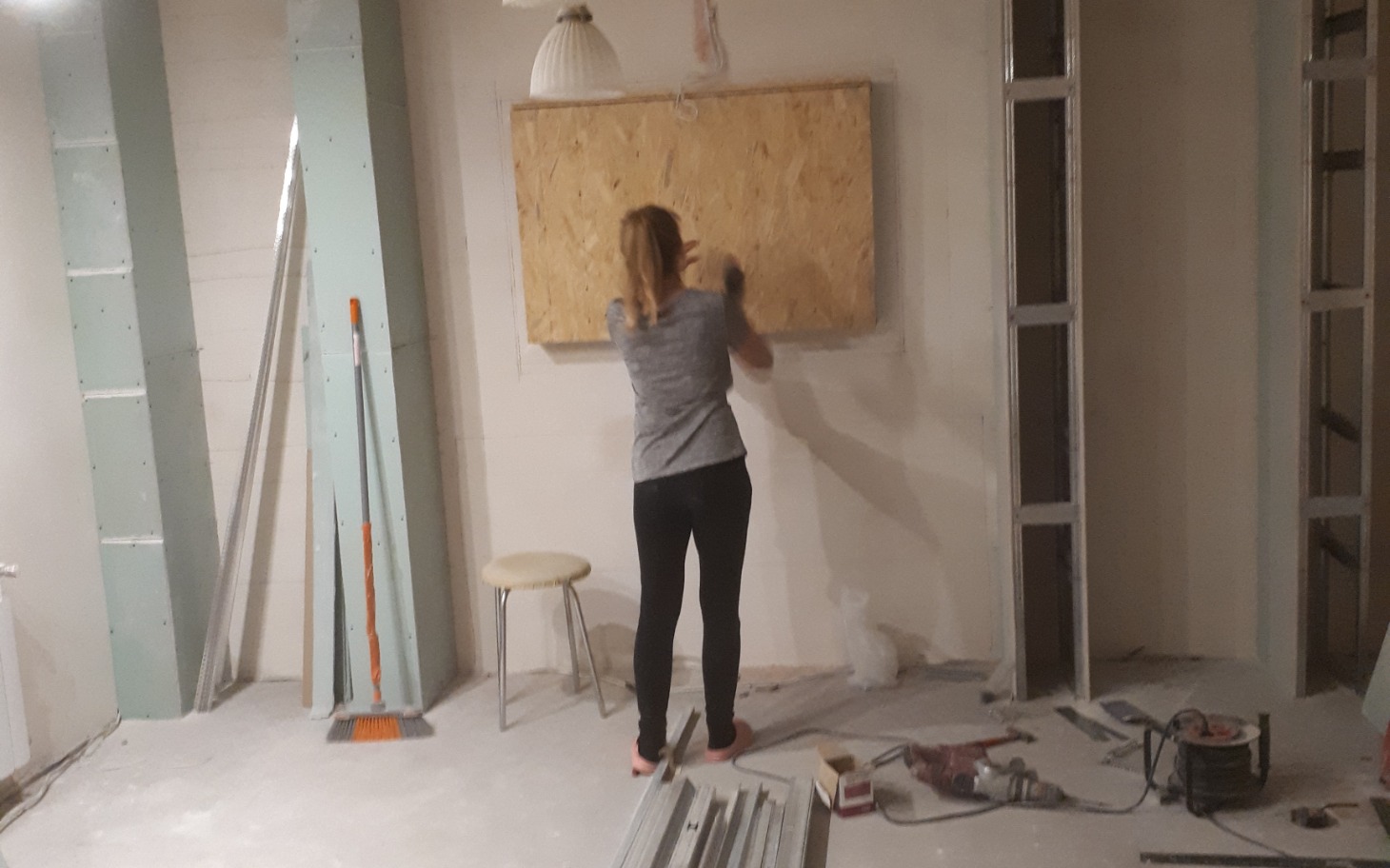 
        Kobieta pracująca nad drewnianą płytą w remontowanym pomieszczeniu.
    