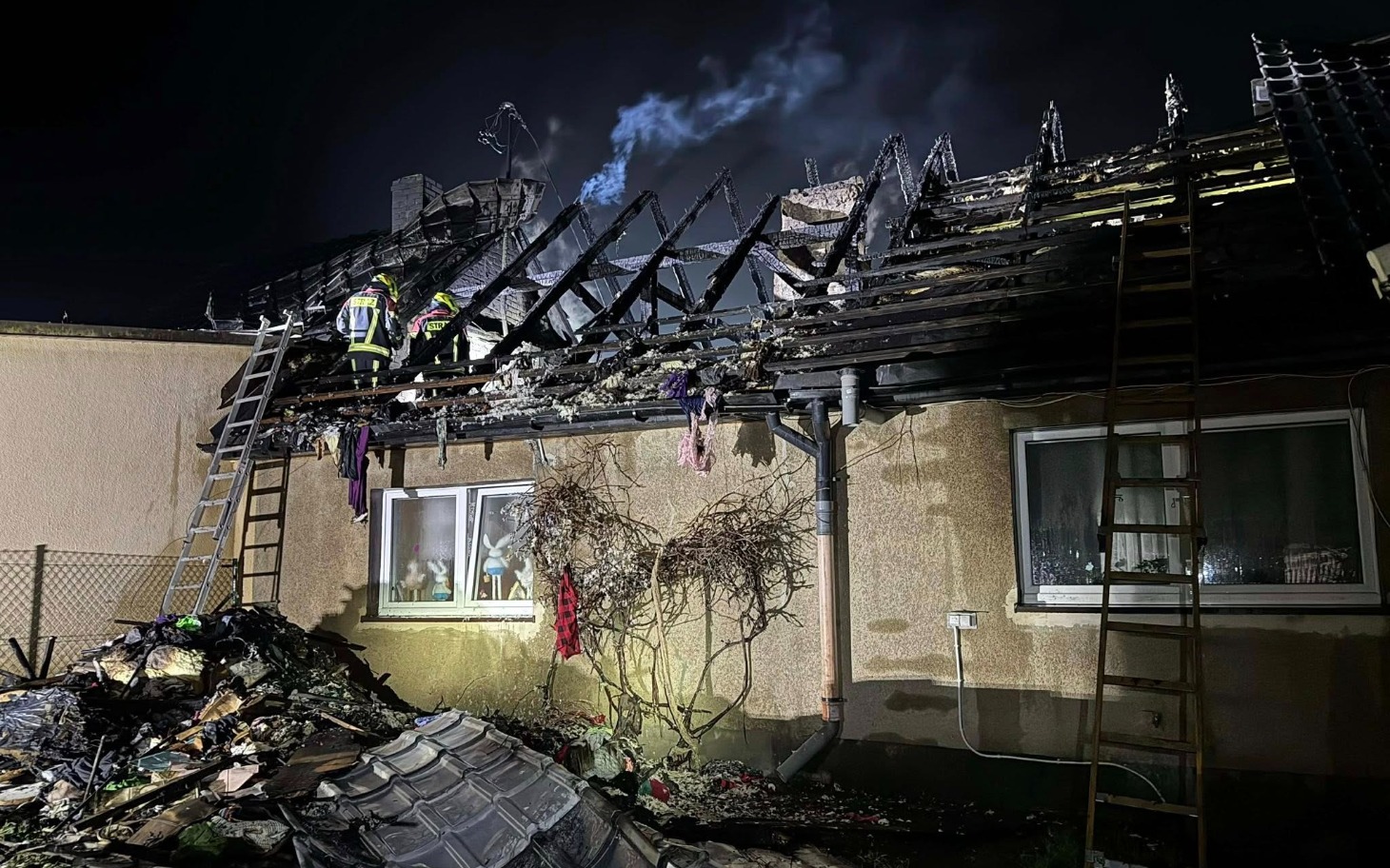 
        Strażacy pracujący przy zniszczonym dachu budynku po pożarze.
    