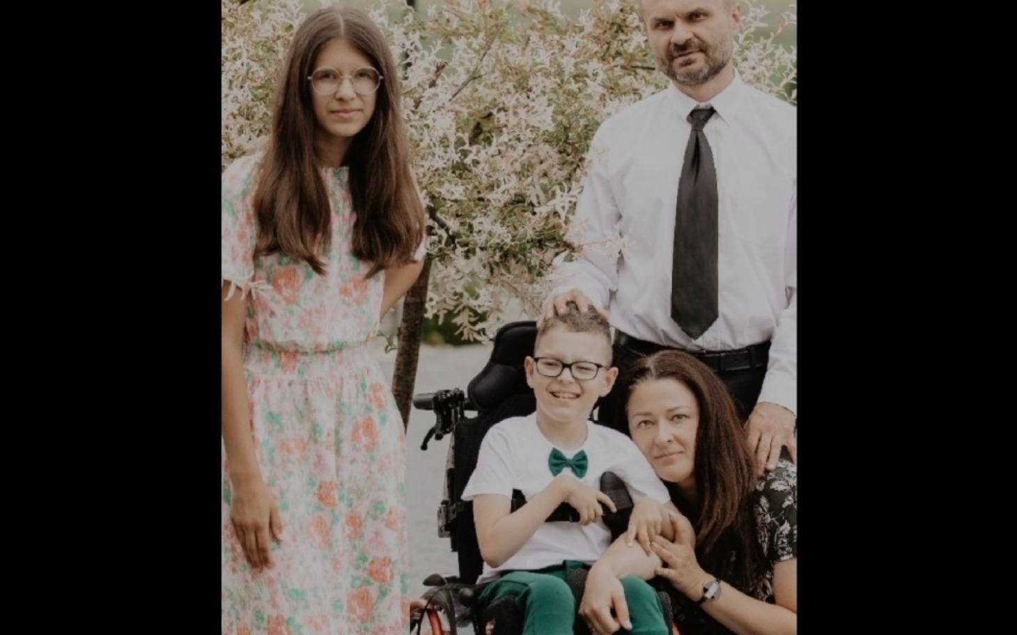 
        Rodzina pozująca w ogrodzie, wśród kwiatów.
    