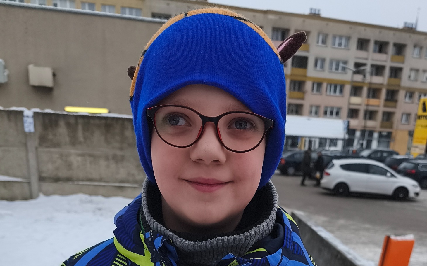 
        Chłopiec w niebieskiej czapce z okularami, uśmiechający się.
    