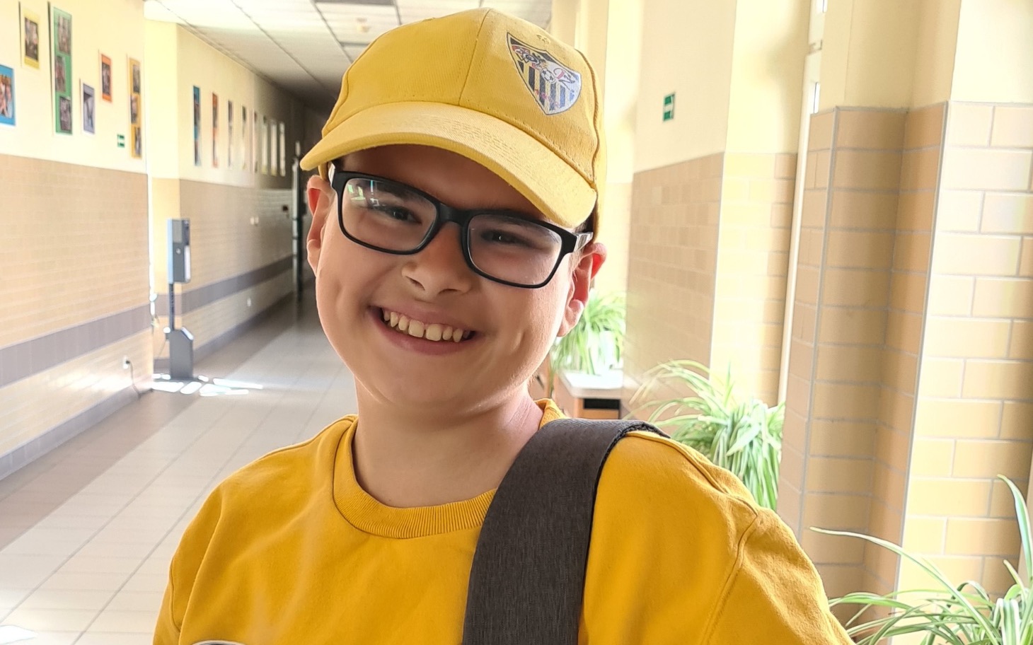 
        Uśmiechnięty chłopiec w żółtej czapce i koszulce, stojący w korytarzu.
    