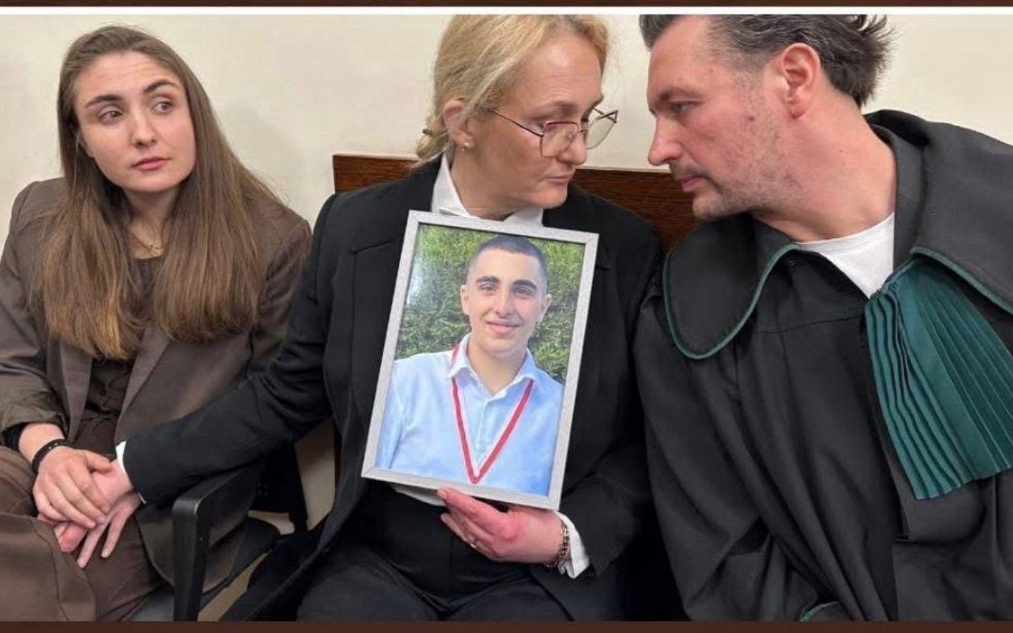 
        Trzy osoby w sądzie, trzymające zdjęcie mężczyzny.
    