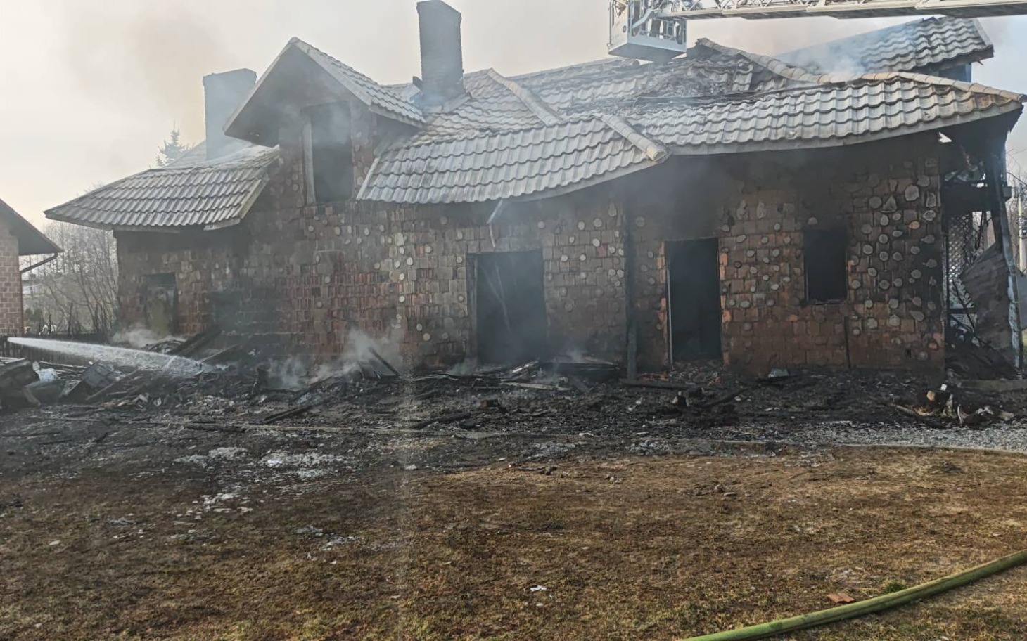 
        Zniszczony dom po pożarze, z dymem unoszącym się w powietrzu.
    