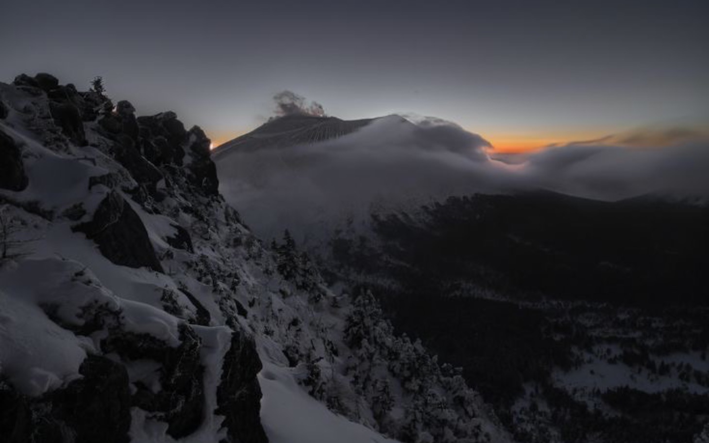 
        Zimowy krajobraz górski z chmurami i zachodem słońca.
    