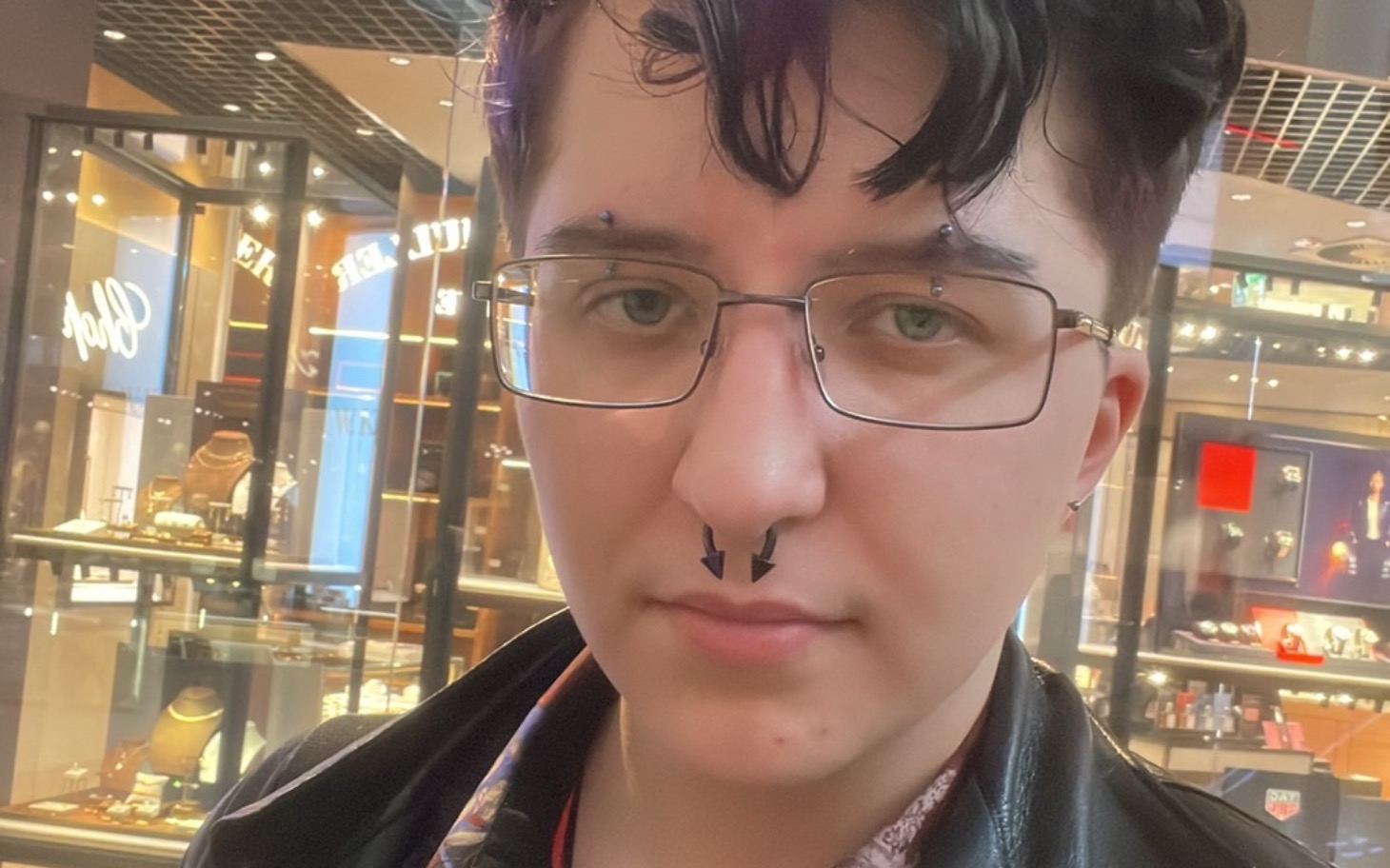 
        Młoda osoba z okularami i kolczykami, patrząca w obiektyw.
    