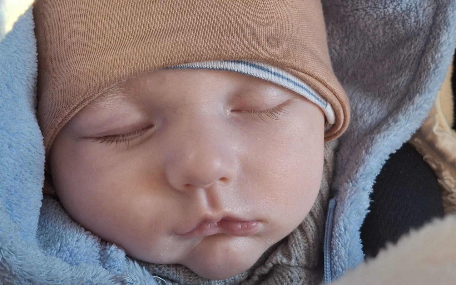 
        Śpiące niemowlę w ciepłym ubranku, z czapką na głowie.
    