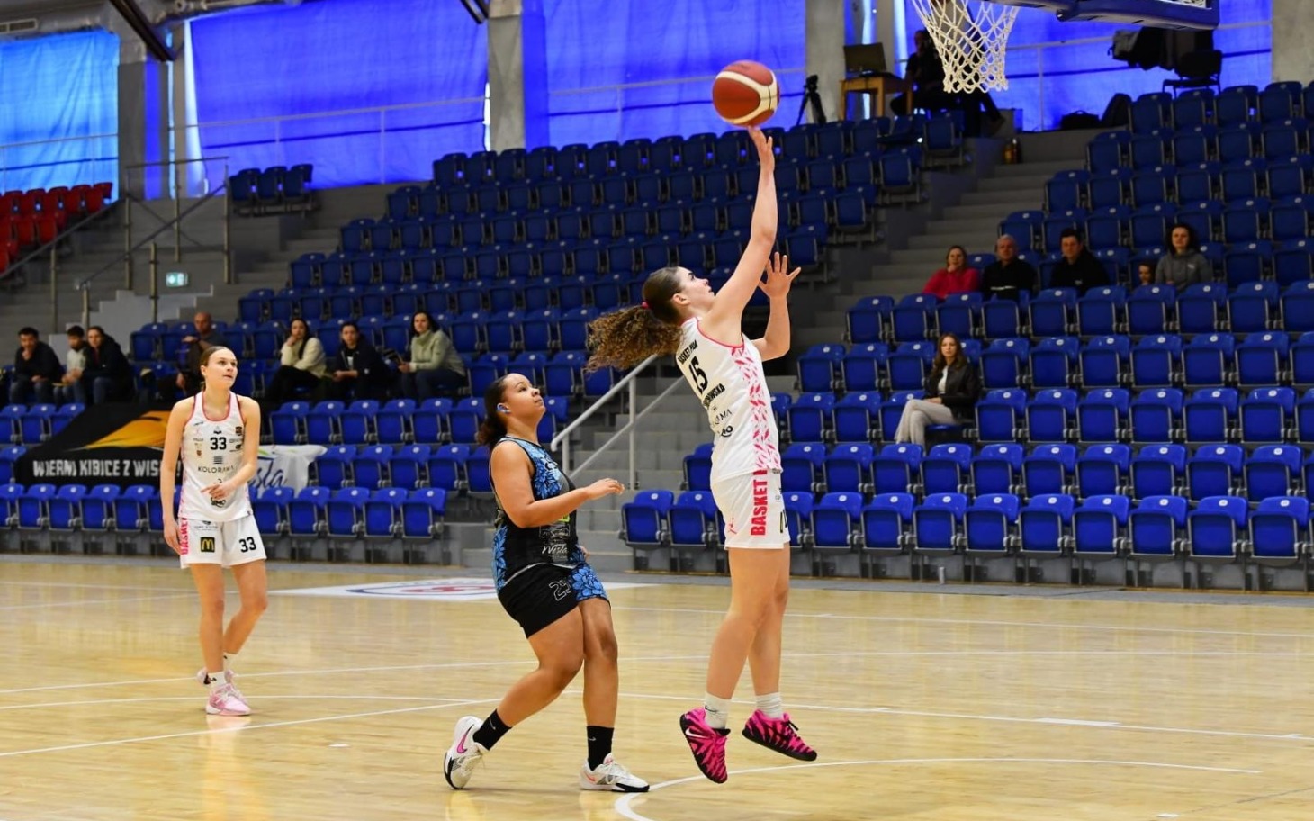 
        Koszykarka wykonująca rzut w trakcie meczu.
    