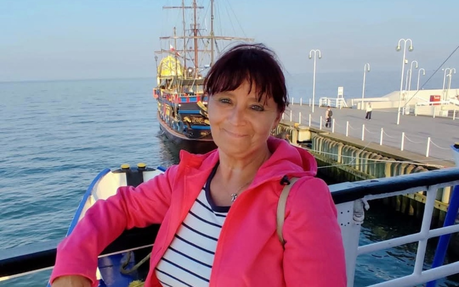 
        Kobieta w różowej kurtce na tle morza.
    