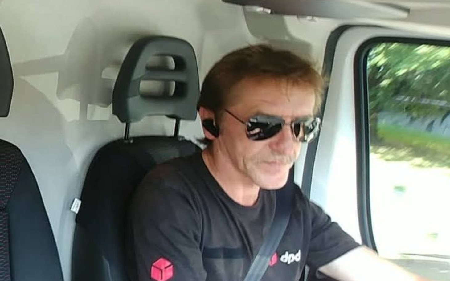 
        Kierowca w samochodzie dostawczym, skupiony na drodze.
    