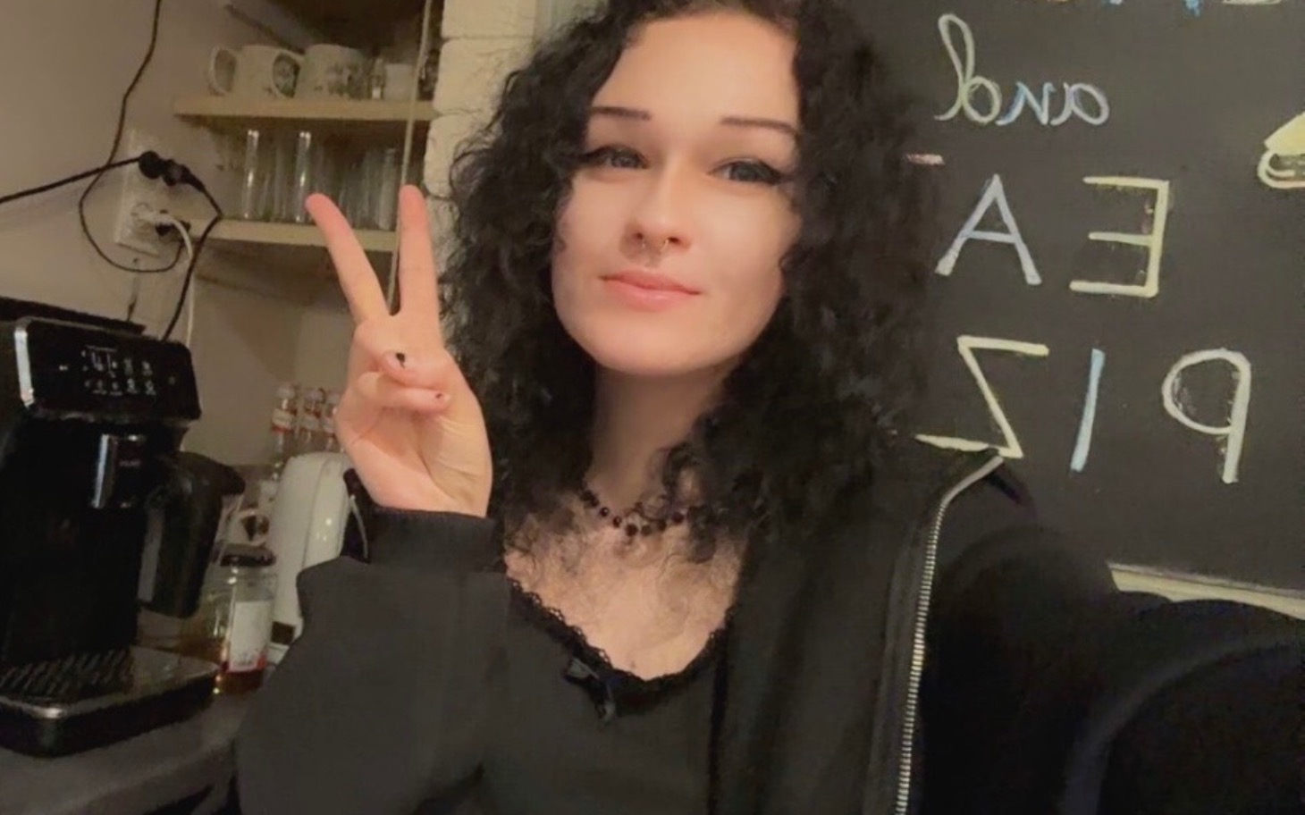 
        Dziewczyna w czarnym ubraniu, pokazująca znak pokoju w kuchni.
    