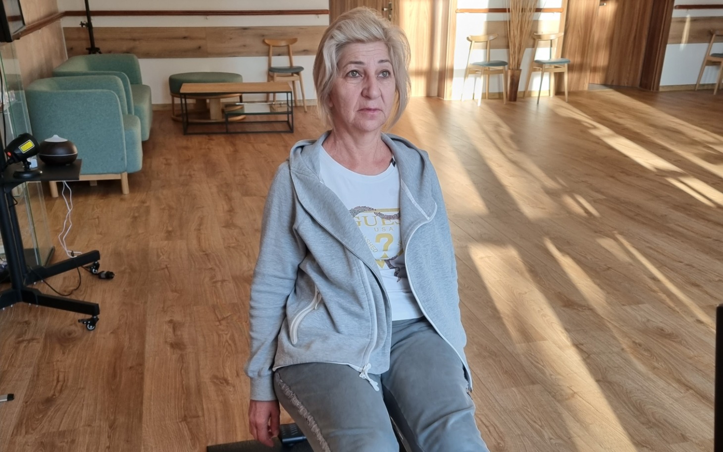 
        Kobieta siedząca w jasnym pomieszczeniu, z wyrazem twarzy pełnym refleksji.
    