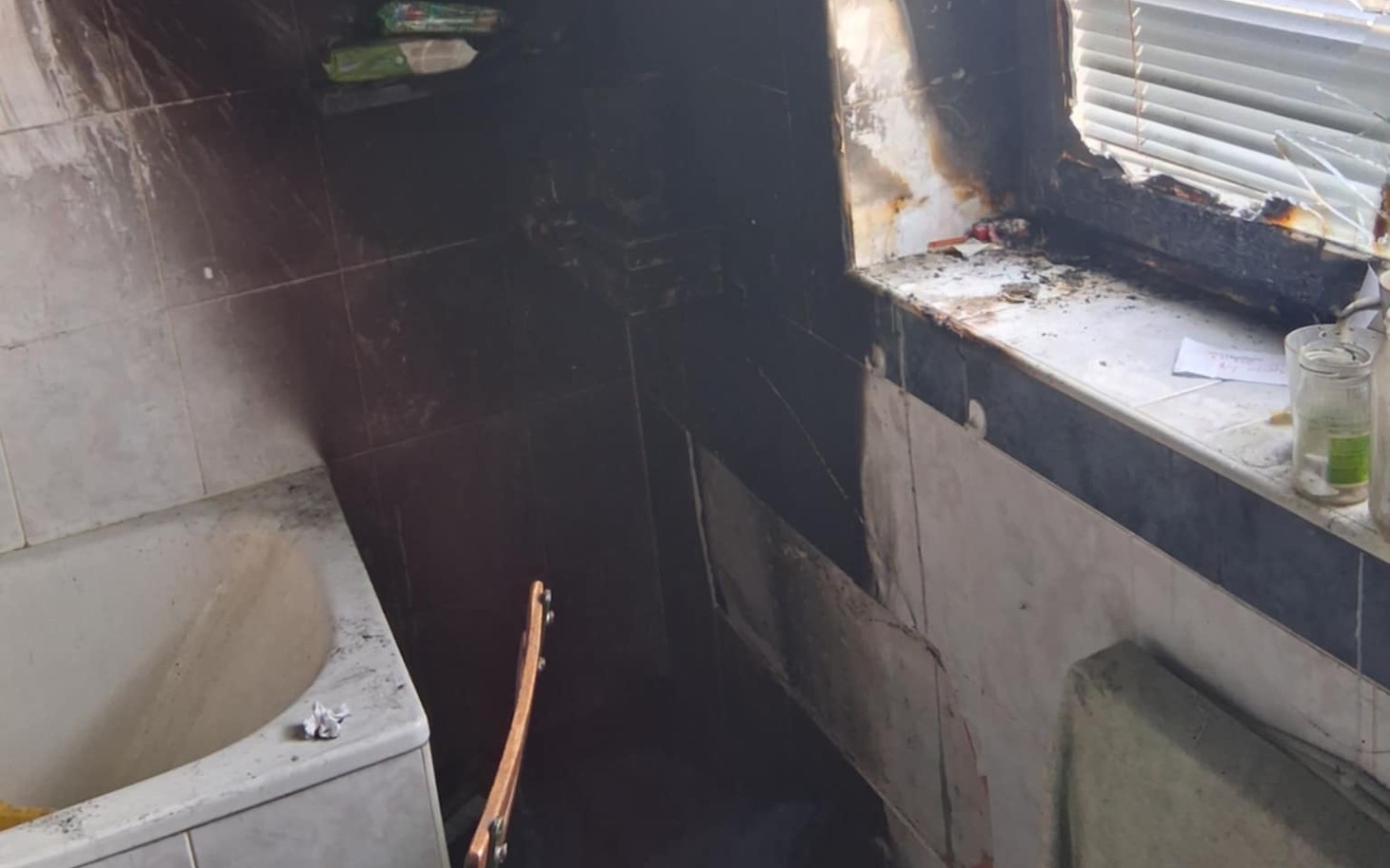 Zniszczona łazienka po pożarze, z popiołem i uszkodzeniami.