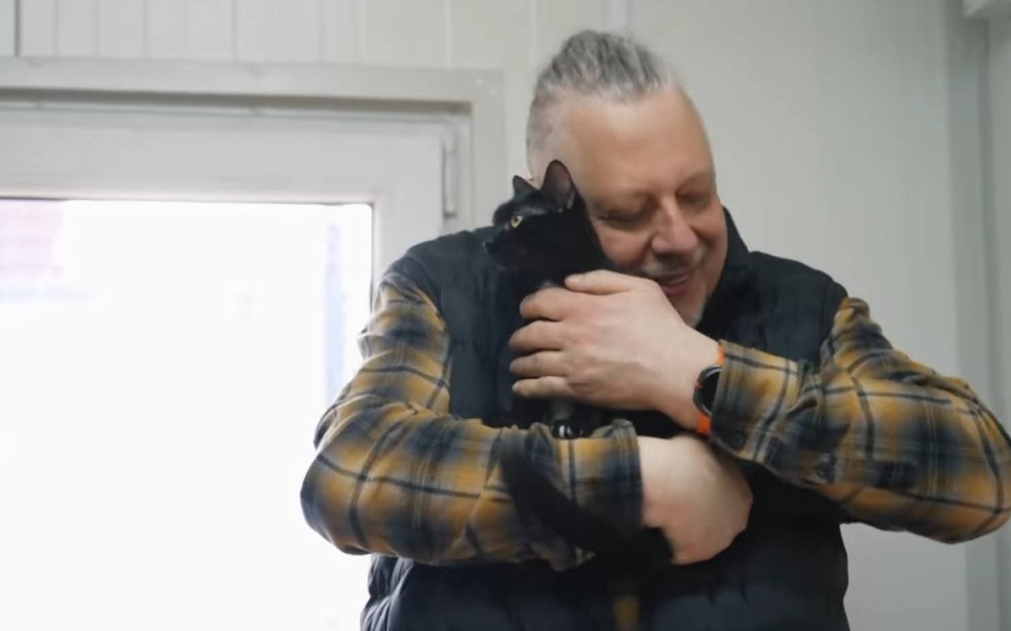 
        Mężczyzna przytulający czarnego kota w pomieszczeniu.
    