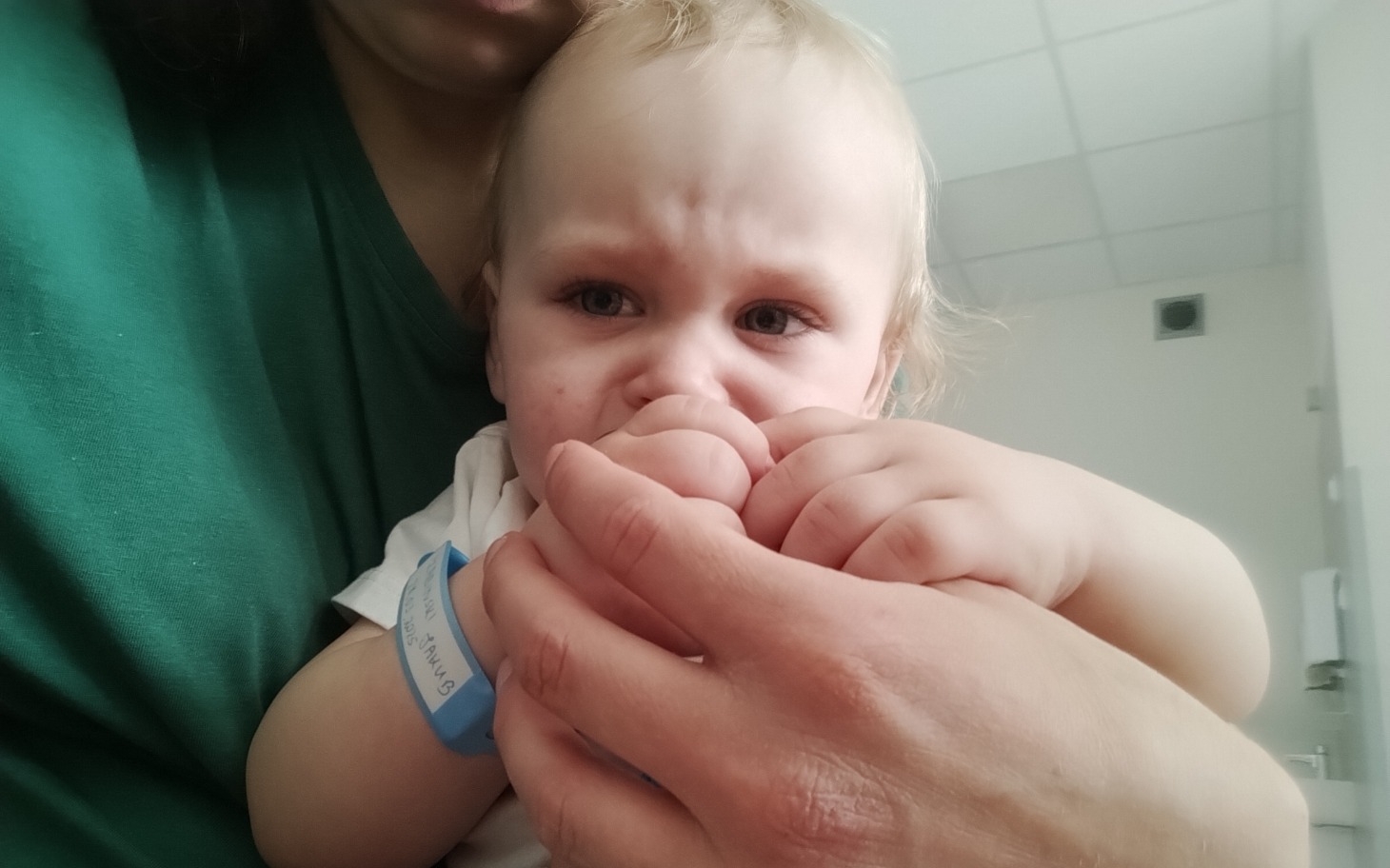 
        Małe dziecko trzymane na rękach, wygląda na zmartwione.
    