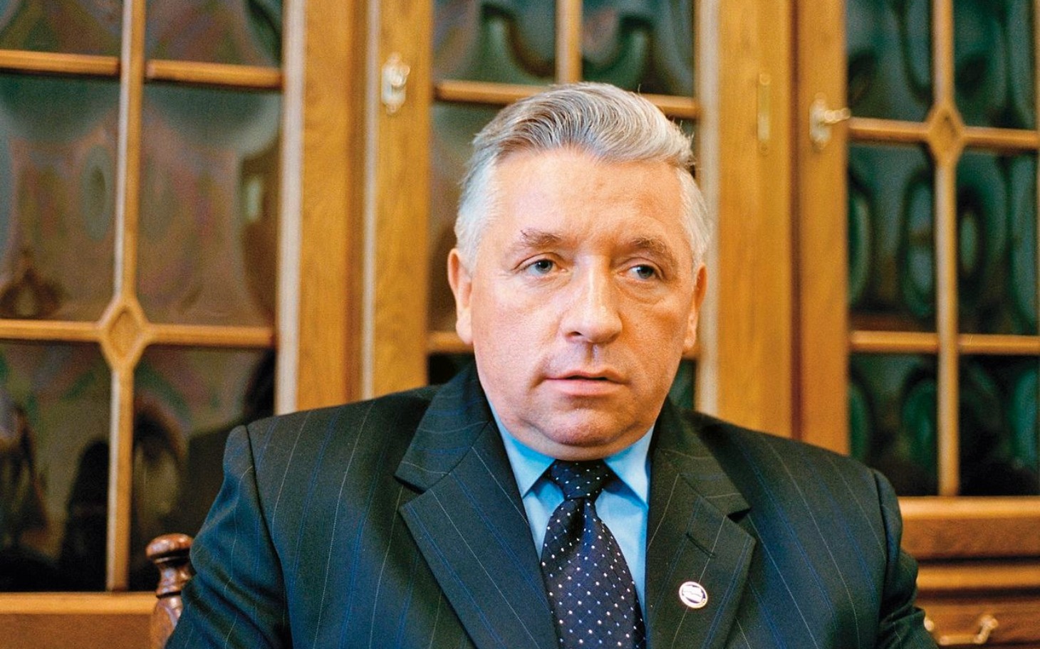 
        Mężczyzna w garniturze, siedzący w biurze, z poważnym wyrazem twarzy.
    