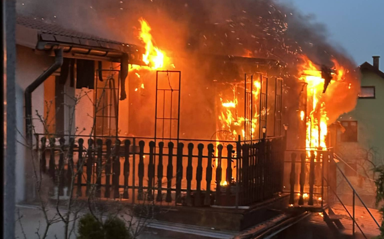 
        Dom w płomieniach, ogień trawi balkon i ściany budynku.
    