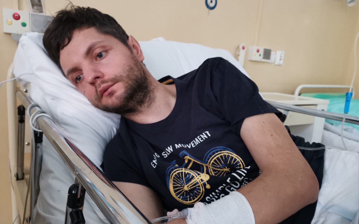
        Mężczyzna leżący w szpitalnym łóżku, z opatrunkiem na ręce.
    