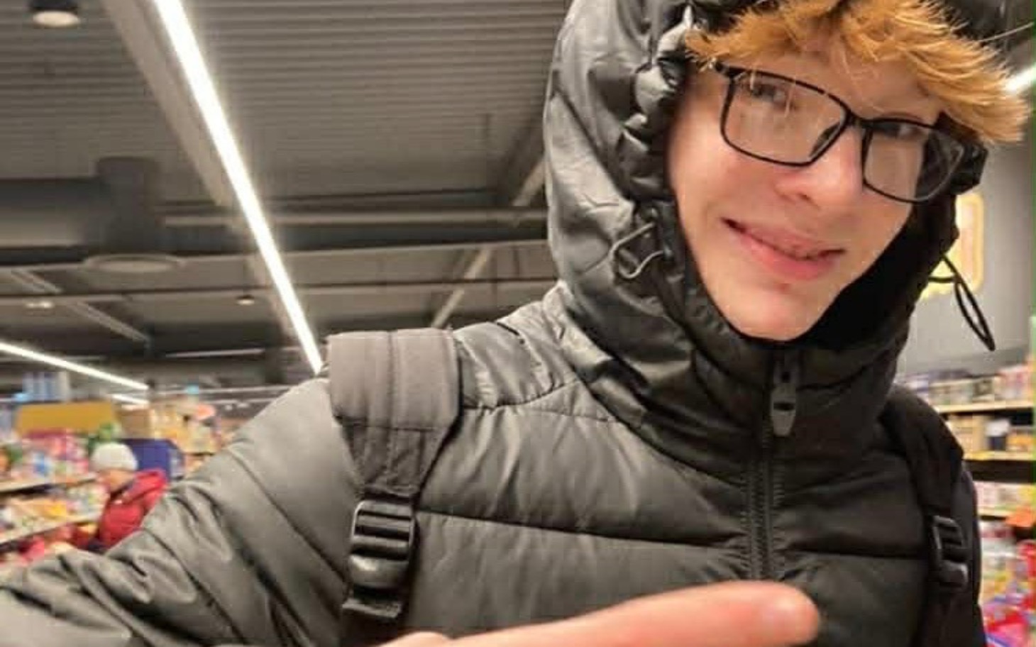 
        Młody chłopak w czarnej kurtce w sklepie, uśmiechający się do kamery.
    