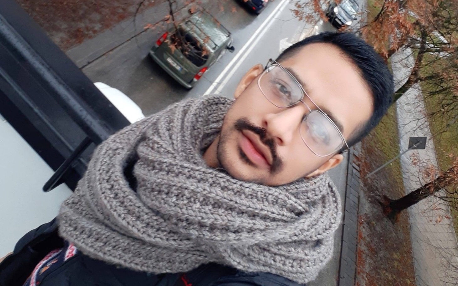 
        Mężczyzna w okularach, uśmiechający się na tle ulicy.
    