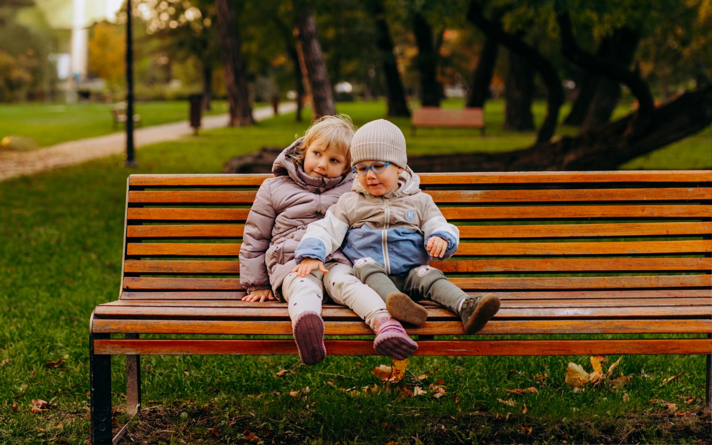 
        Dwie dziewczynki siedzące na ławce w parku.
    