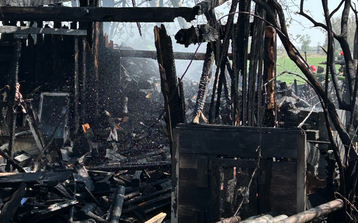 
        Zgliszcza po pożarze, zniszczony budynek w tle.
    