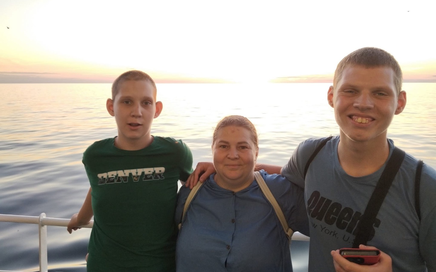 
        Rodzina pozująca do zdjęcia na tle zachodzącego słońca nad wodą.
    