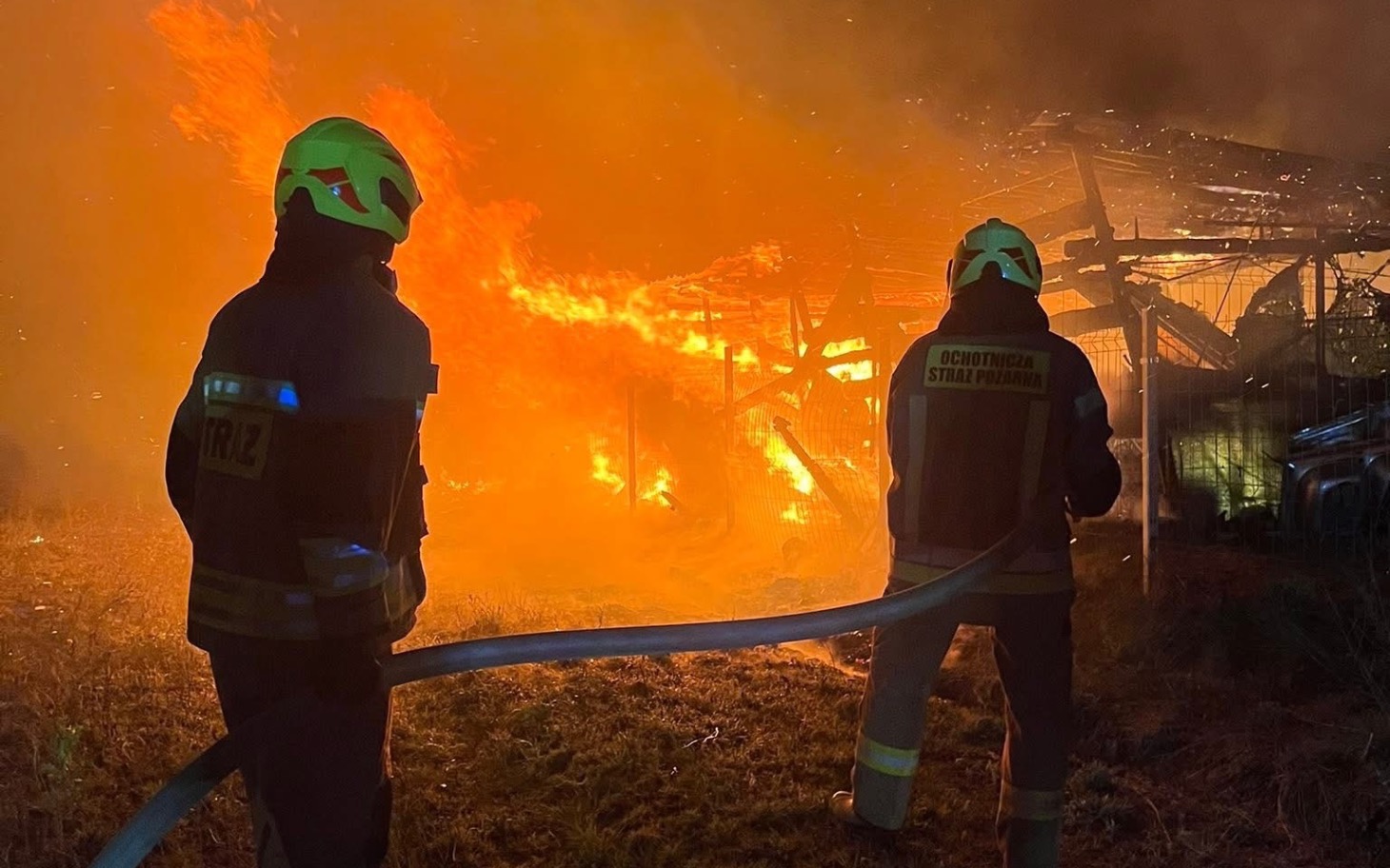 
        Strażacy walczą z pożarem w tle, otoczeni przez ogień.
    