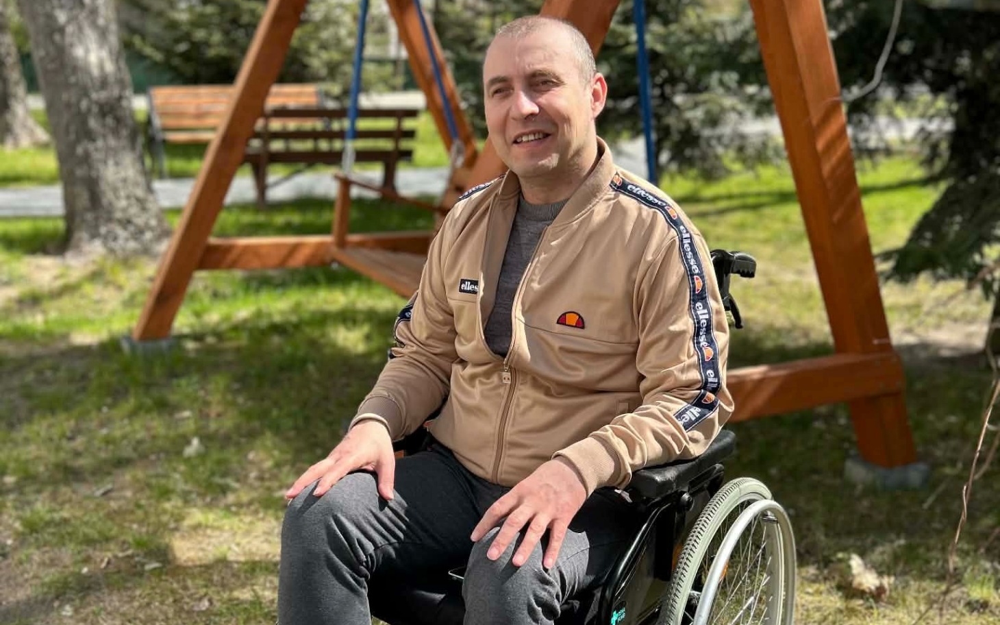 
        Mężczyzna na wózku inwalidzkim, uśmiechnięty w parku.
    